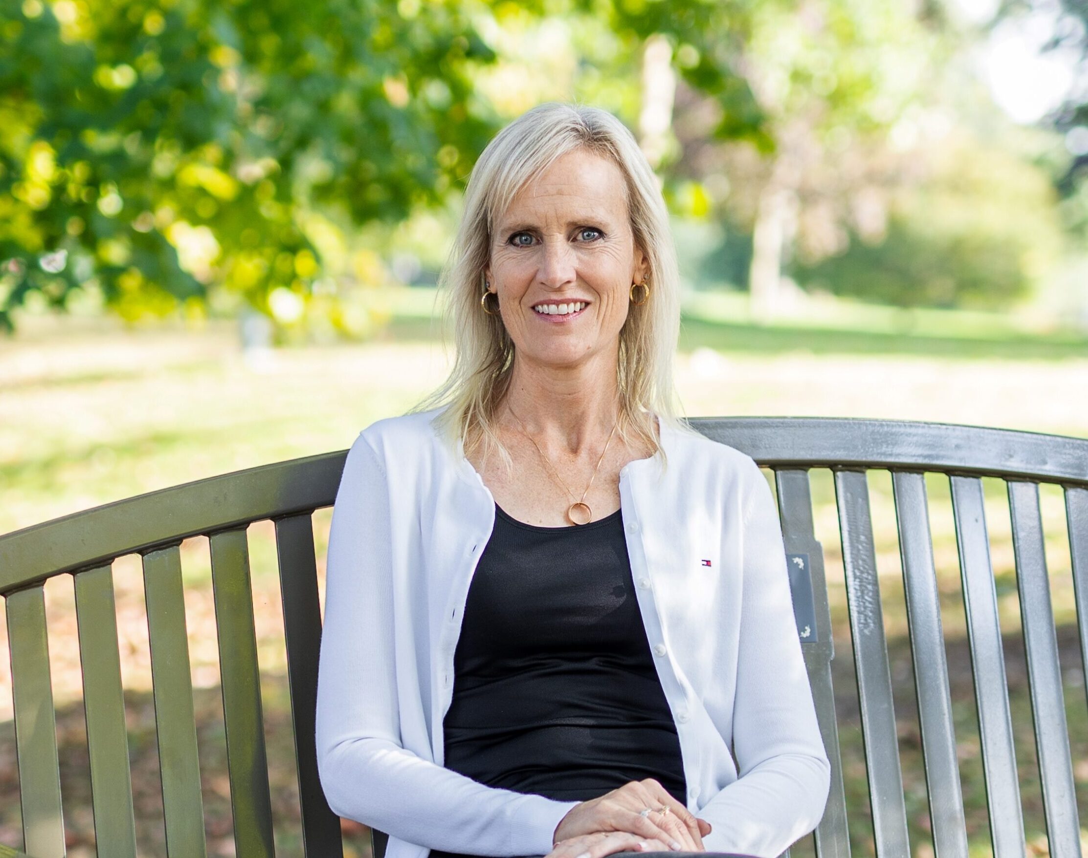 Cheryl Vanderveen sitting on a bench in a park on a sunny day smiling at the camera